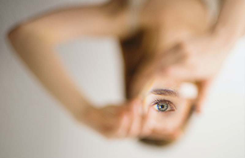 Foto einer jungen Frau, ihr Gesicht ist teilweise durch ihre Hände verdeckt